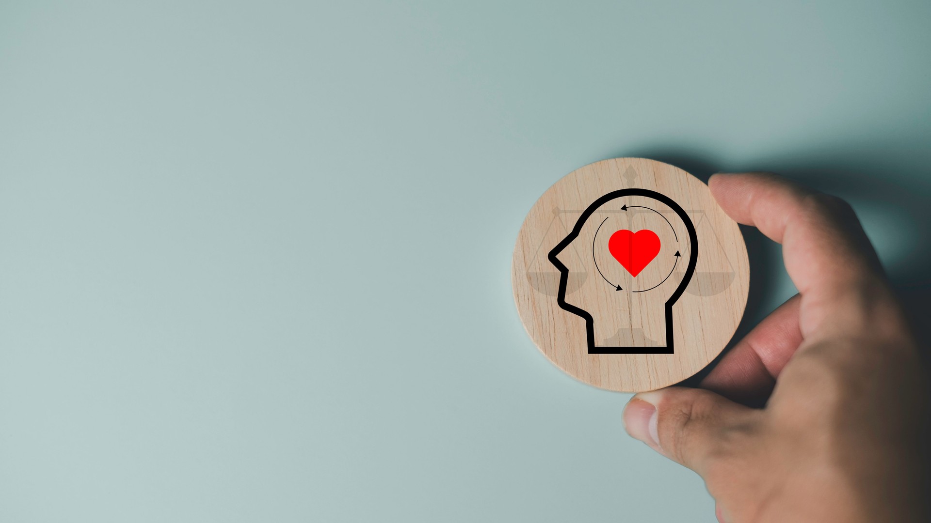 Ethics and emotional intelligence concept showing a hand holding a wooden circle with a human head outline and heart symbol, representing moral values, empathy, and mindfulness inside the human mind.